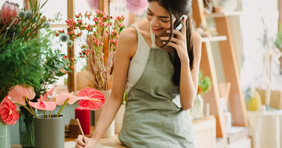 Dueña de una floristería sonríe mientras atiende un pedido por teléfono en el mostrador