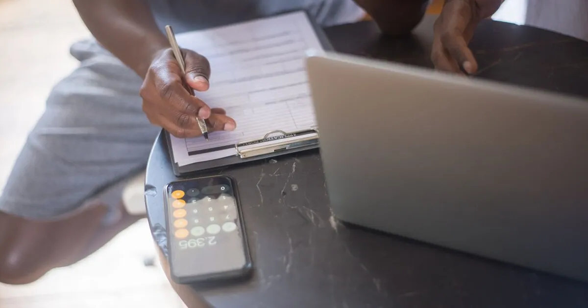 Una persona anota en una planilla junto a una calculadora y una notebook, comparando opciones